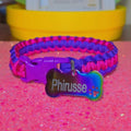 Paracord bracelet with a colorful tag on a pink surface, with a blurred background of toys.